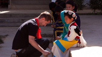 IBM Corporate Service Corps - Team China 18 - Yunnan Province, China. Our deployment included a visit to Runan Wan, a primary school deep in the foothills of rural Yunnan. During our visit we showed the students how to conduct some simple science experiments, and taught them games and sporting events from our home countries. In this photo, Martin Hagovsky (IBM Slovakia) helps two Naxi girls prepare for the three-legged race.